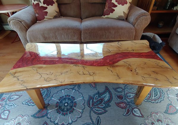 An epoxy river table with a red-pigmented river vein.